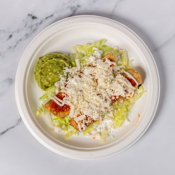 Two taquitos topped with red sauce, sour cream, and cotija cheese, served with guacamole and lettuce.