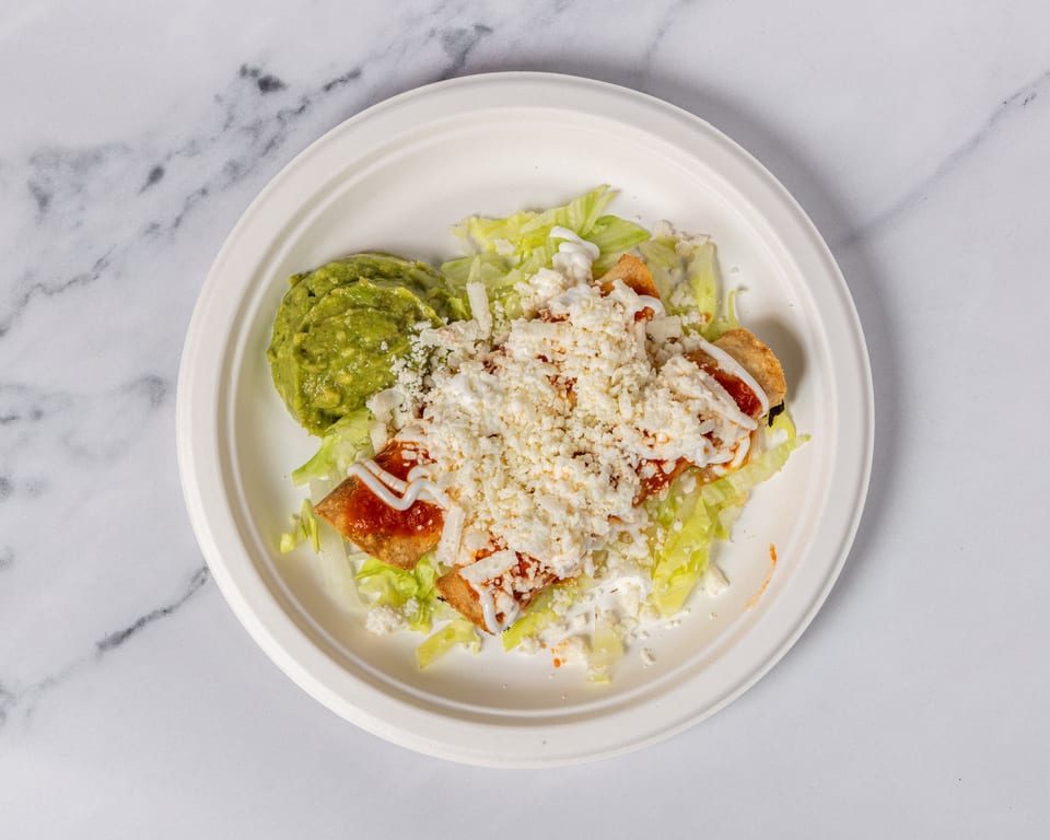 Two taquitos topped with red sauce, sour cream, and cotija cheese, served with guacamole and lettuce.