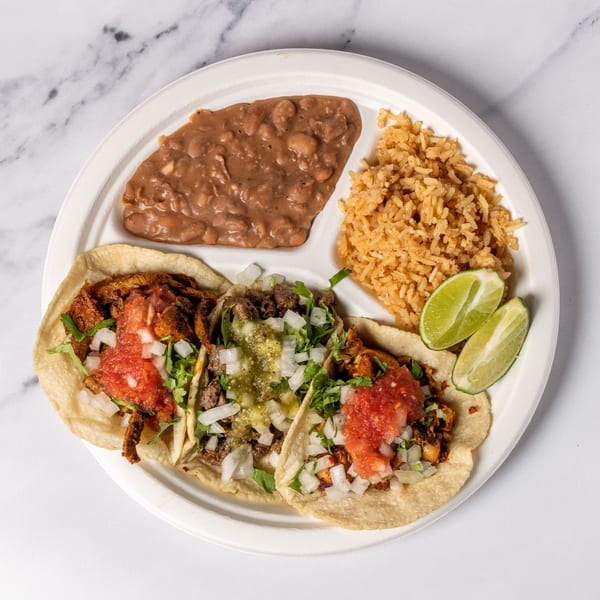 Three tacos with various toppings, rice, and beans on a white plate with lime wedges.
