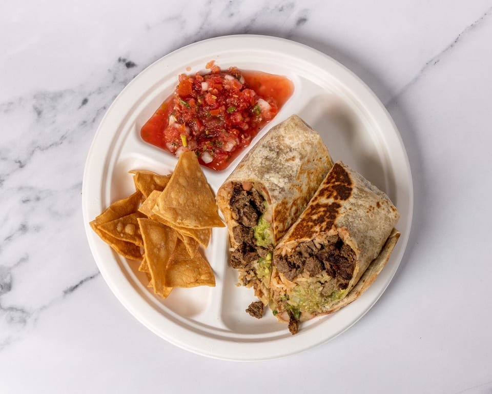 Two burritos with steak, rice, and guacamole, served with tortilla chips and salsa on a white plate.