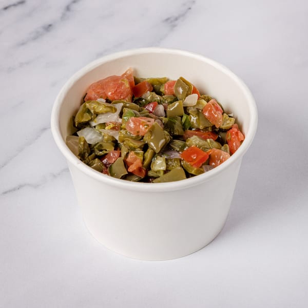 Nopalitos salad with diced cactus, tomatoes, and onions in a white bowl on a marble surface.
