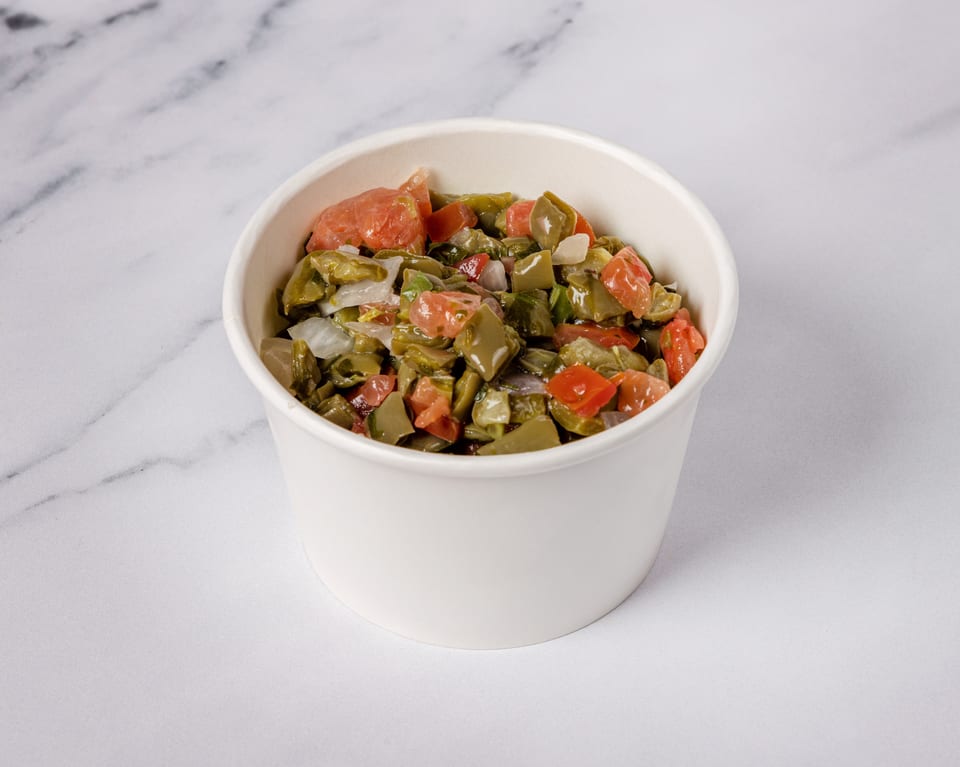 Nopalitos salad with diced cactus, tomatoes, and onions in a white bowl on a marble surface.