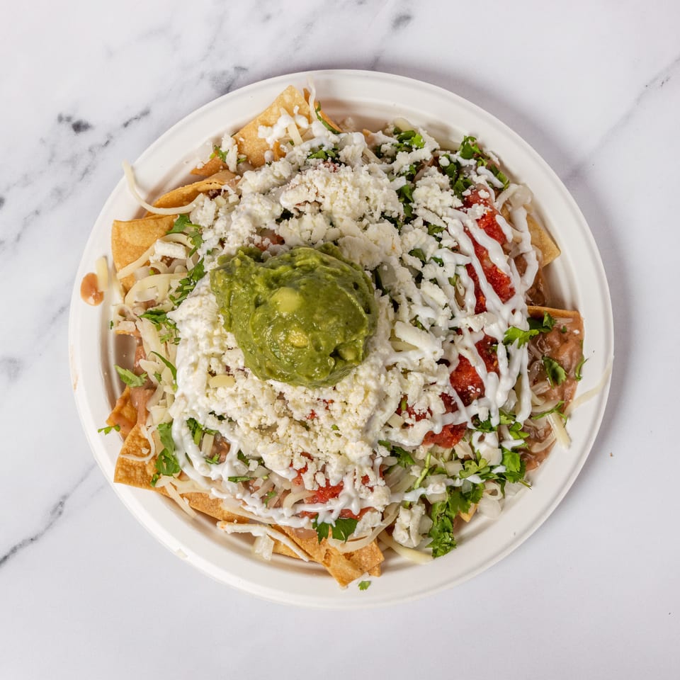 Overhead view of a plate of nachos with guacamole, cheese, salsa, and sour cream.
