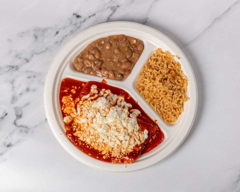 A divided plate with enchiladas, rice, and beans on a white marble surface.