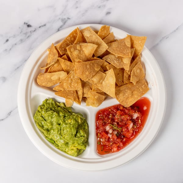 A white divided plate holds crispy tortilla chips, guacamole, and fresh salsa on a marble surface.