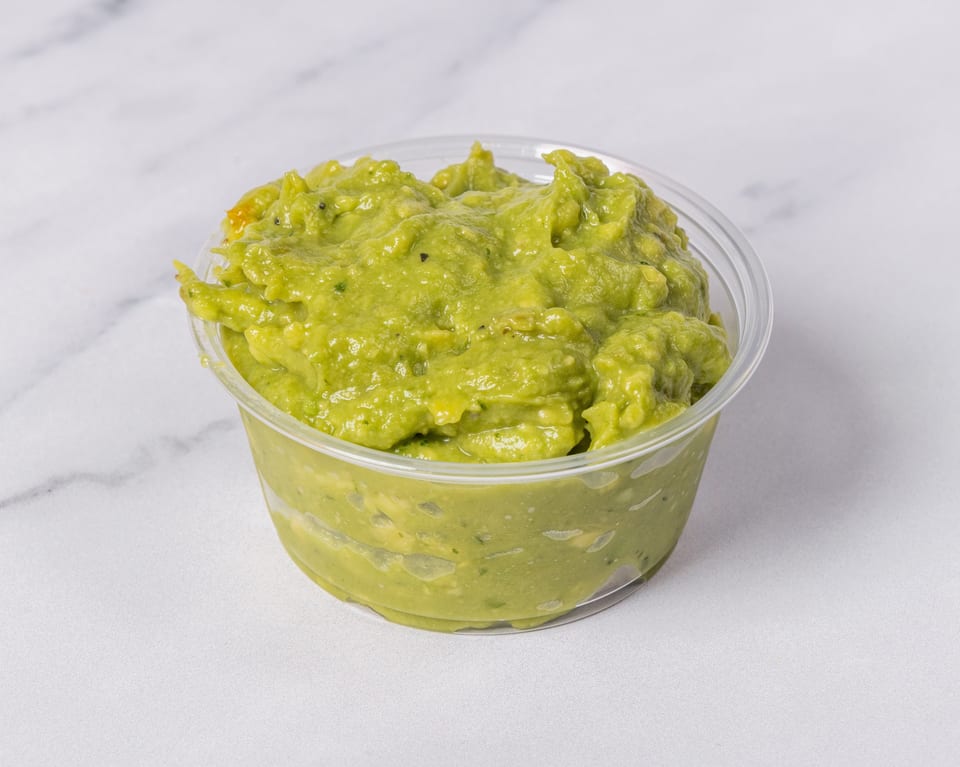 A clear plastic container filled with chunky green guacamole on a white marble surface.