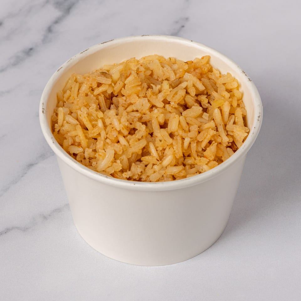 A white paper cup filled with golden-brown fried rice, set against a white marble background.