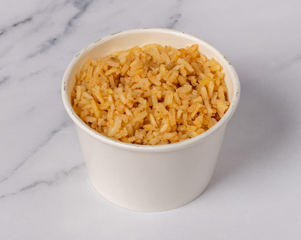 A white paper cup filled with golden-brown fried rice, set against a white marble background.