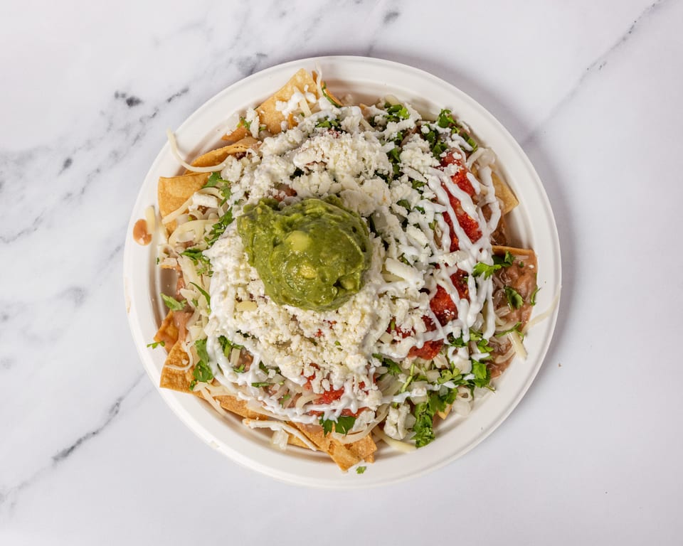 Overhead view of a plate of nachos with guacamole, cheese, salsa, and sour cream.