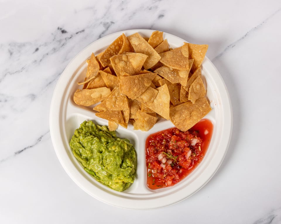 A white divided plate holds tortilla chips, guacamole, and salsa on a marble surface.