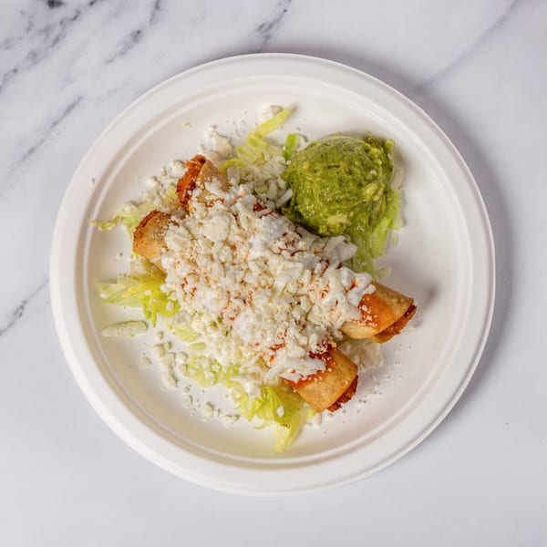 Two taquitos topped with cheese and sauce, served with guacamole and lettuce on a white plate.