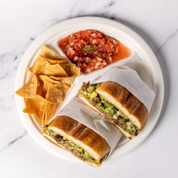 Two torta sandwiches with chips and salsa on a white plate, on a marble surface.