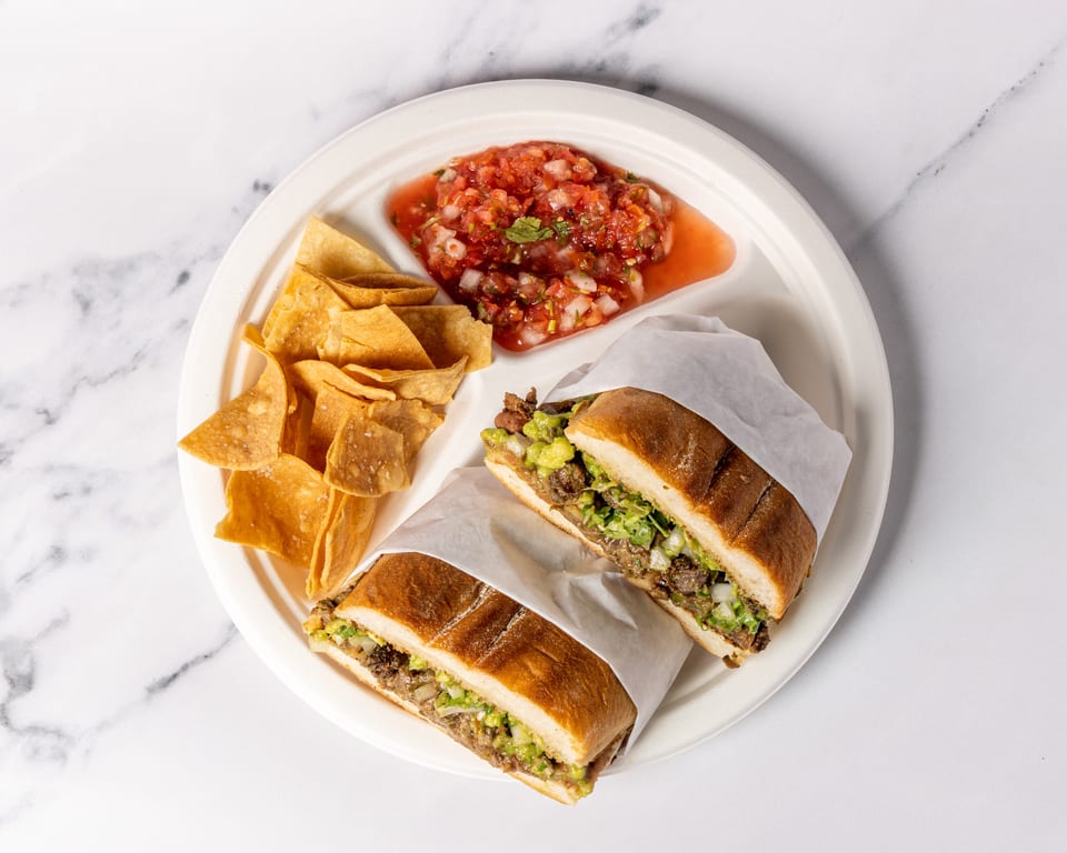 Two torta sandwiches with chips and salsa on a white plate, on a marble surface.