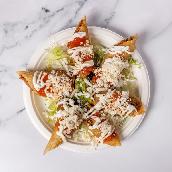 Six taquitos arranged in a star shape, topped with red sauce, sour cream, and cheese.